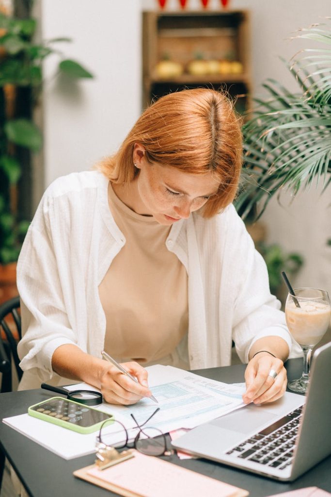 privatlan Kvinna som analyserar finansiella dokument för att ansöka om ett privatlån, med hjälp av laptop och miniräknare.
